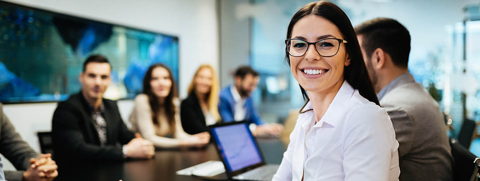 A smiling woman in glasses stands in front of a group of people, conveying a sense of joy and engagement